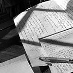 Handwritten papers and pen in the shadow of a window pane.